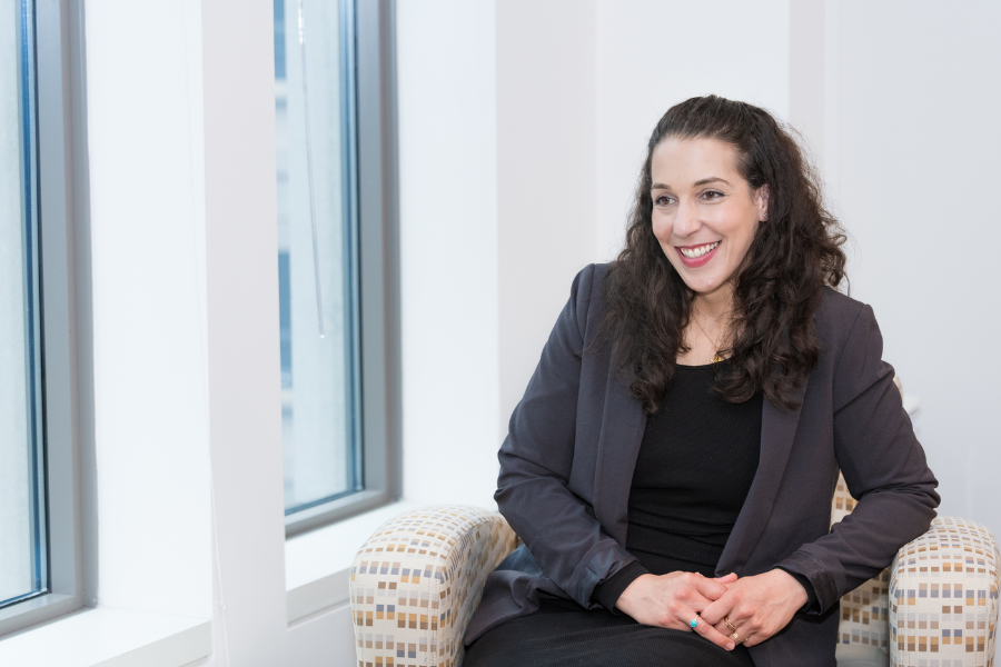 Nadia Abuelezam seated in a chair, facing a window and smiling.