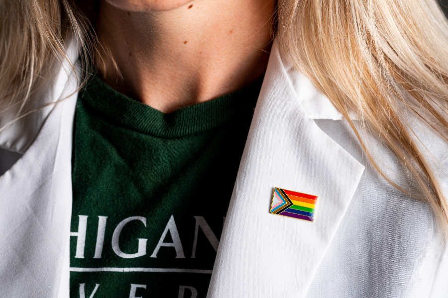 A closeup of a LGBTQIA+ pin on a white coat with an MSU shirt underneath.