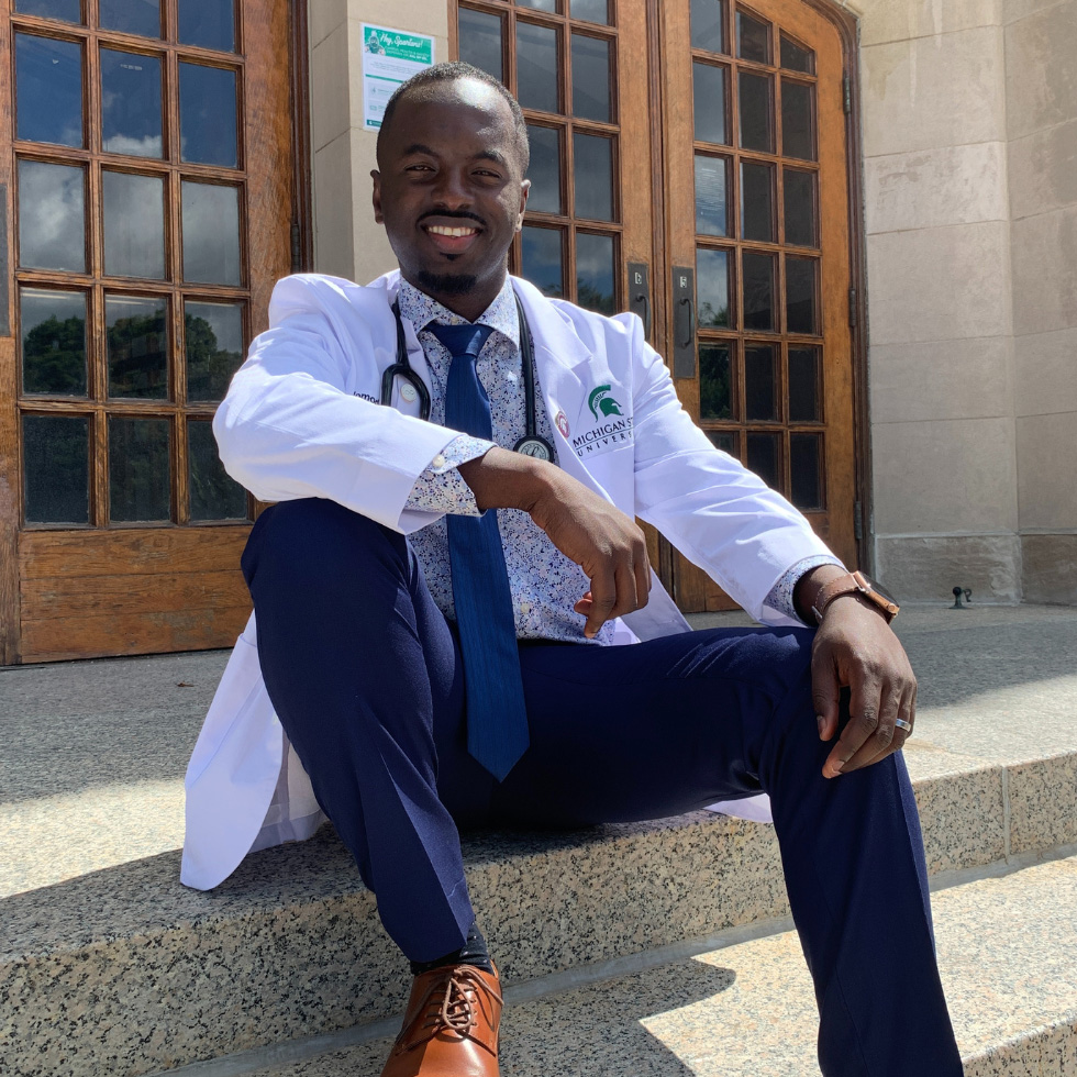 Momodou Bah in his white coat sitting on some steps.