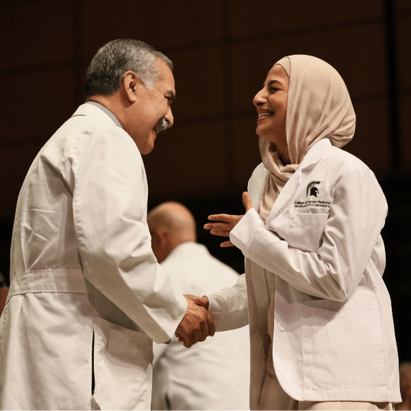 A student displaying immense happiness in their white coat.