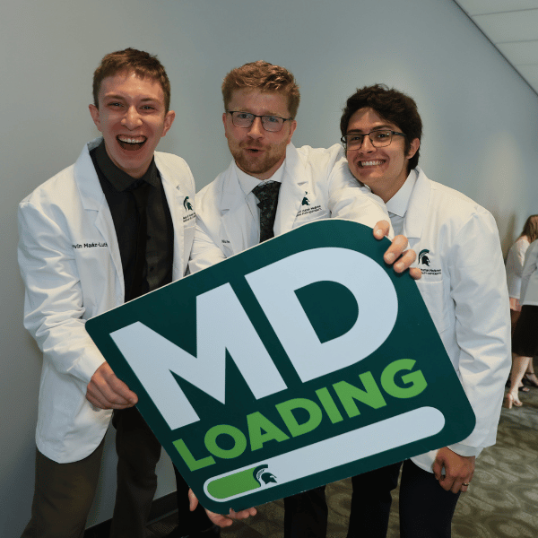 Three students holding an "MD loading" sign with pure joy on their faces.