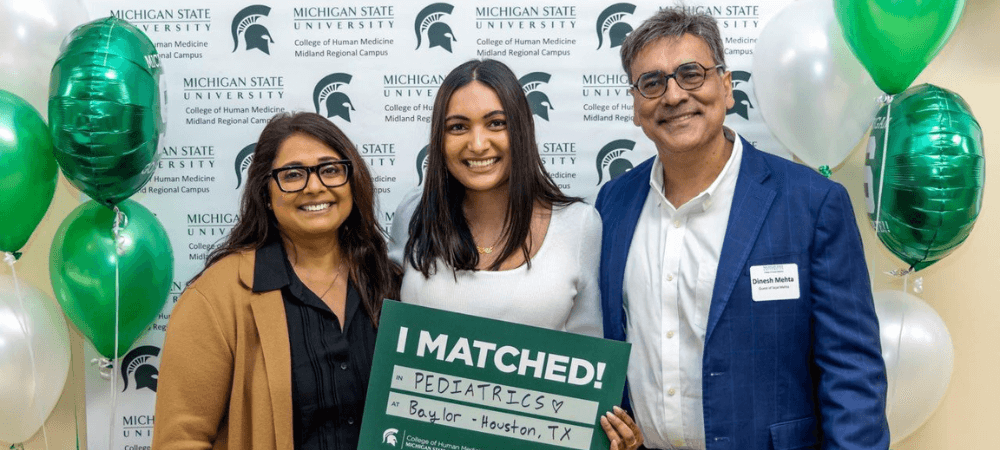 Sejal and parents holding a match day sign.