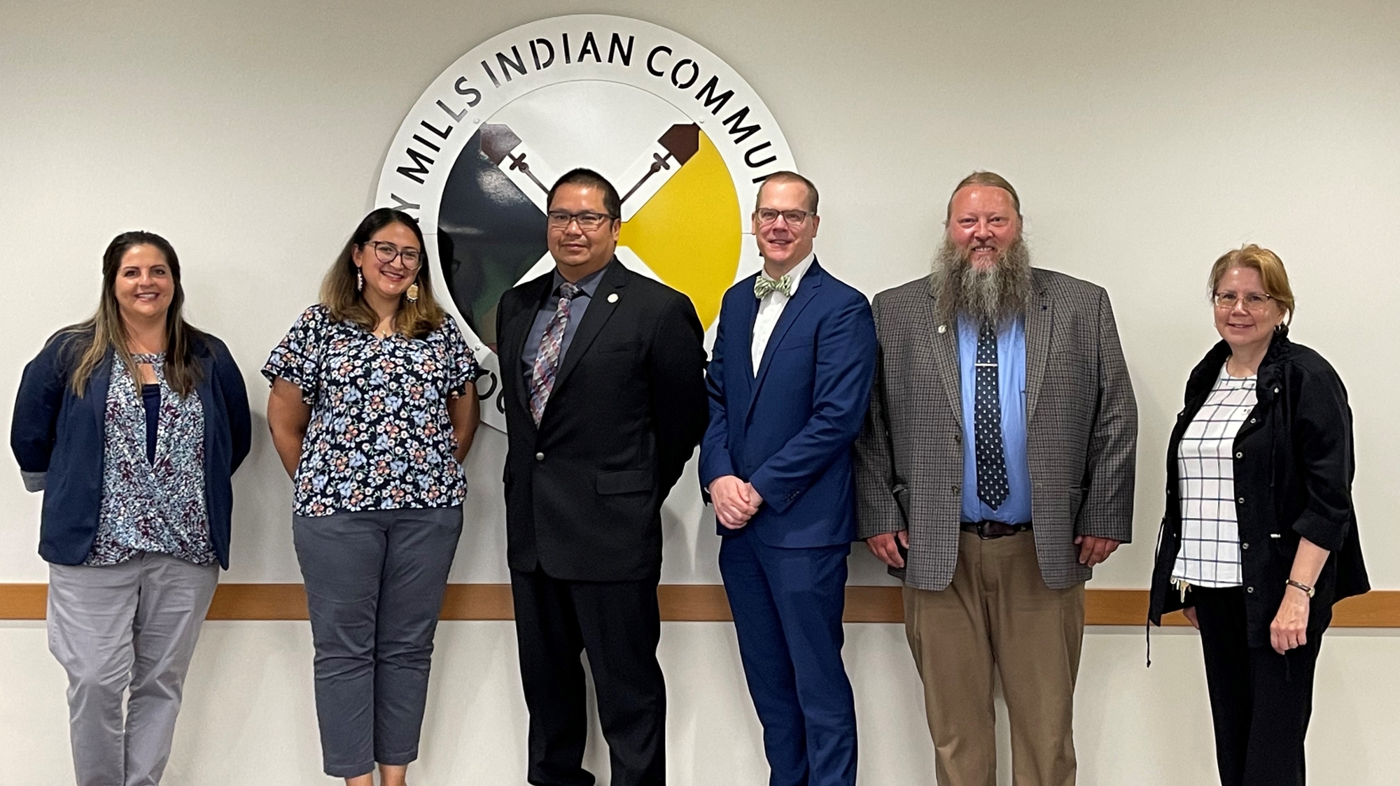 Six people pose for camera in front of a sign that reads Bay Mills Indian Community