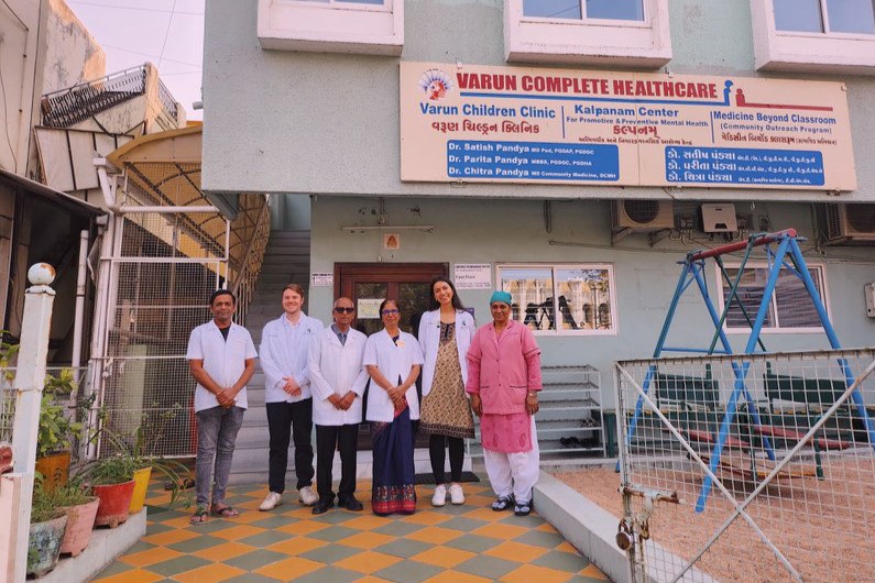 A group of six people stand in front of Varun Complete Healthcare, a light green building with a sign above the entrance.