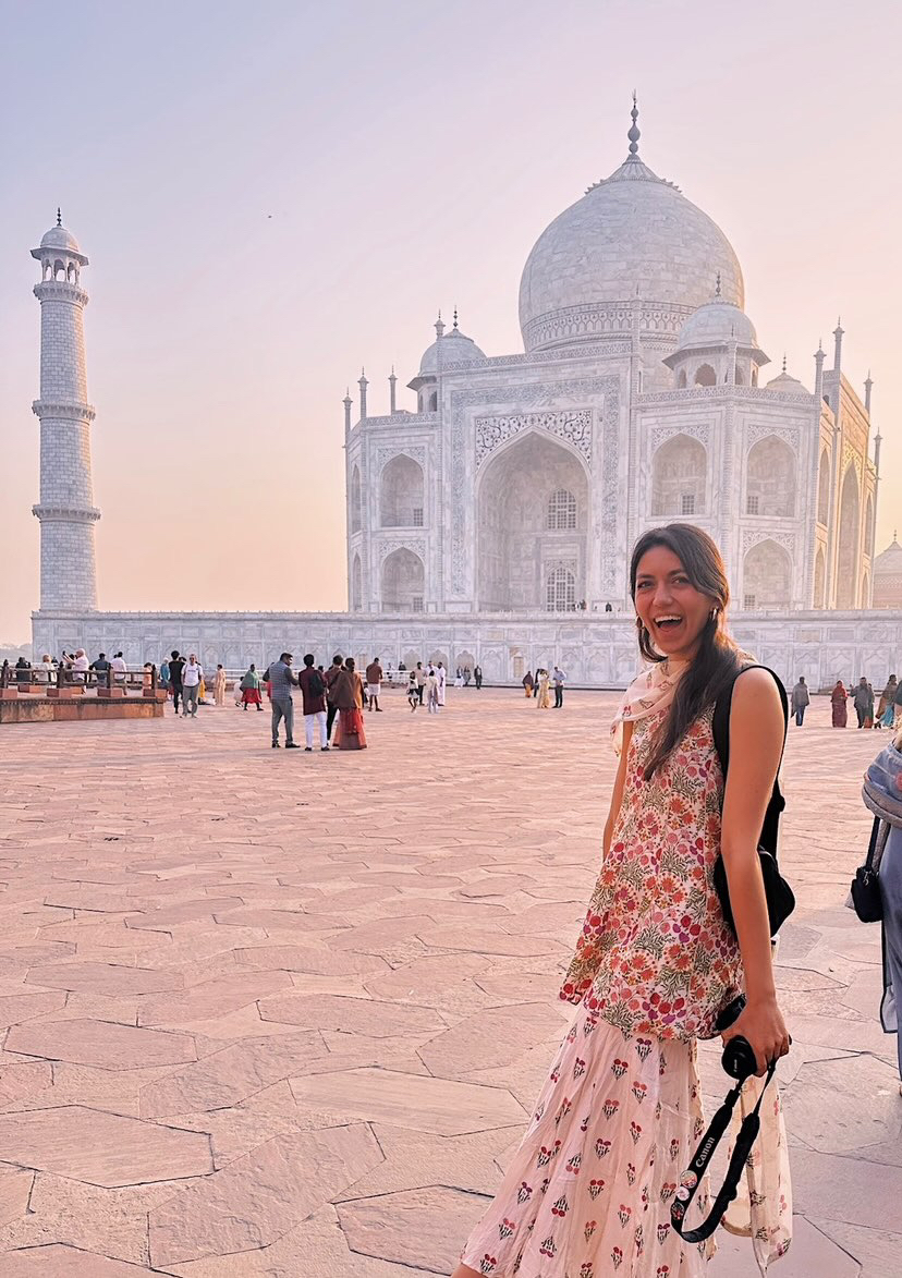 A woman smiling at the Taj Mahal during sunset.