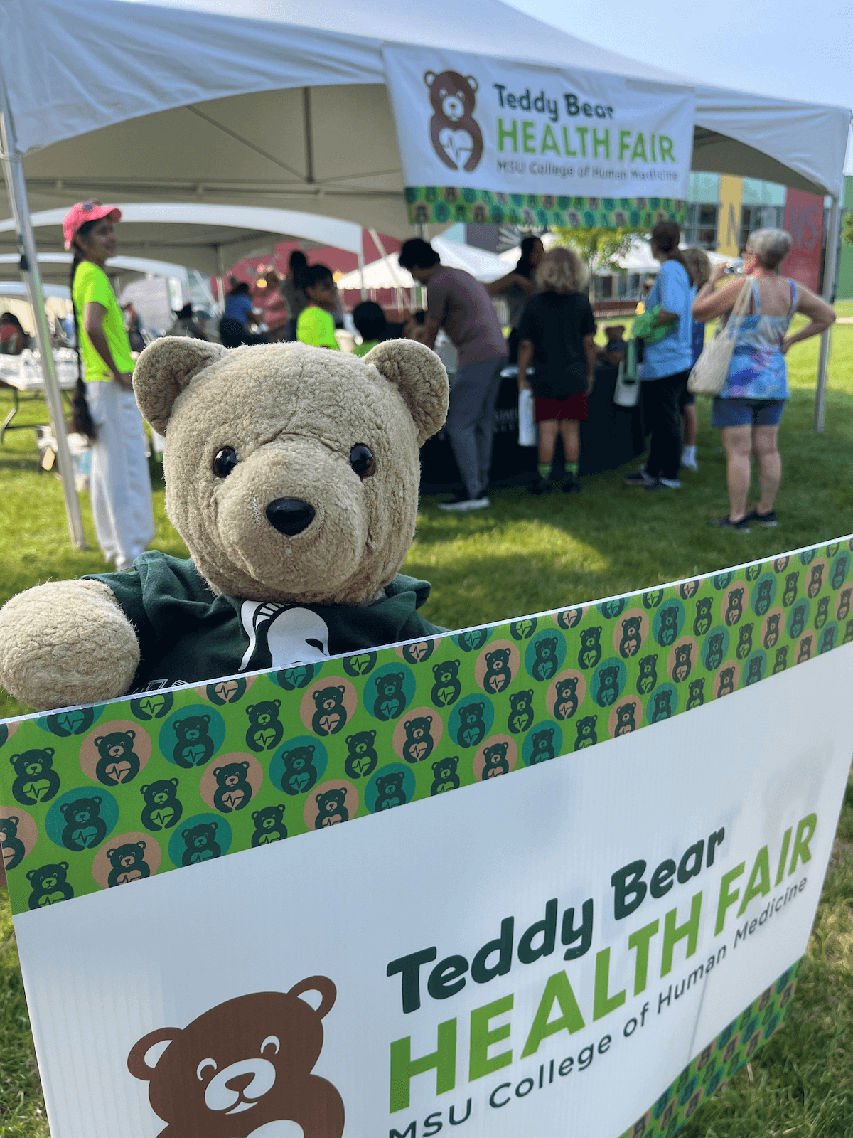 Hope Bear standing next to a Teddy Bear Health Fair sign.