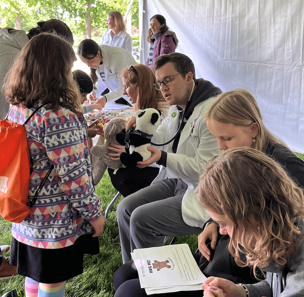 Drs. Olga Napolova and Harrietta Christodoulos from the Department of Pediatrics and Human Development, Shems Hamdan (MS2), Nora Mertz-Bynum (MS3), Alexander Bynum (MS3) and two high school students attend to young humans and their stuffies.
