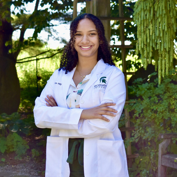 Photo of student Monica Hill standing in white coat with arms crossed