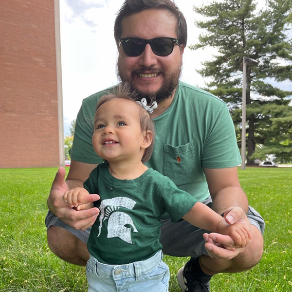Student Joseph Mariscal holds daughter, who is wearing a green tshirt with a sparty helmet