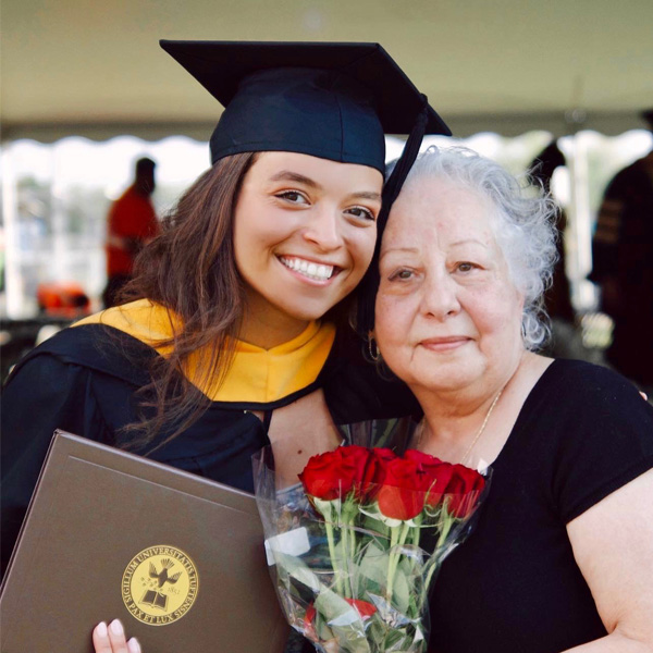 Student Seraphima Sidhom poses with family member wearing graduation gown and holding flowers